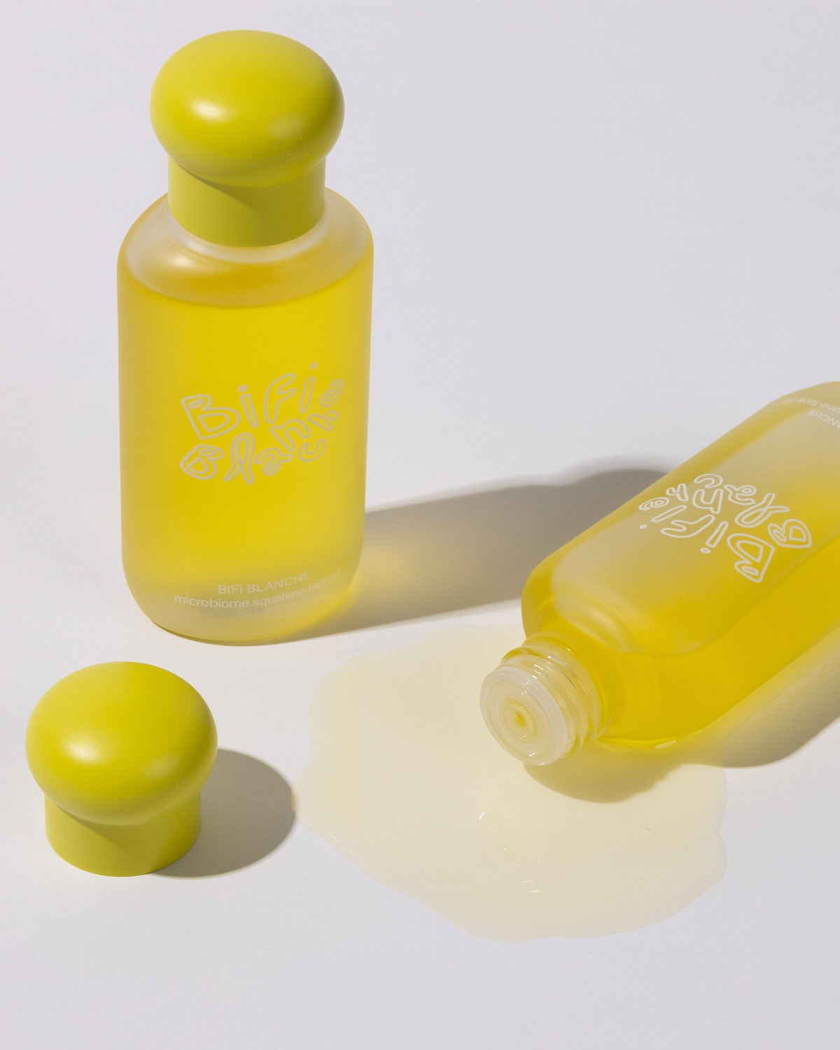 An open bottle of Bifi Blanche Microbiome Squalane Face Oil tipped over with yellow liquid pooling on the surface.