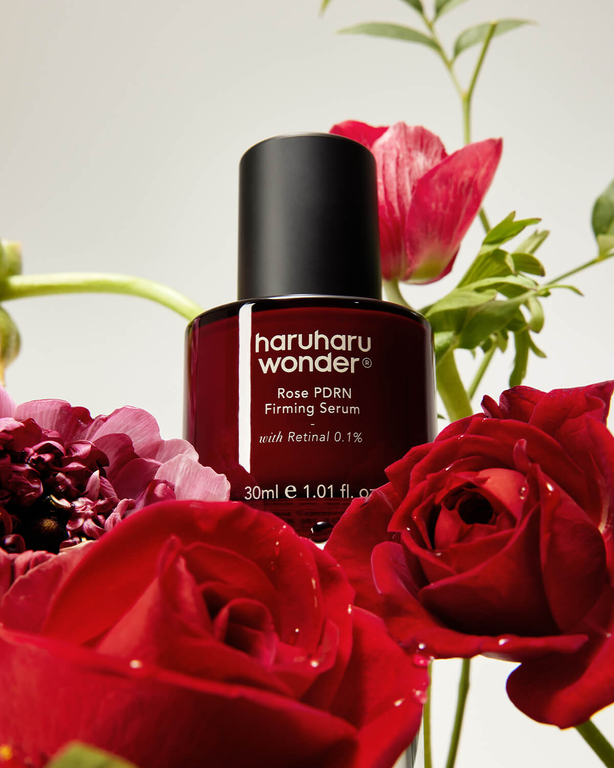 Haruharu Wonder Rose PDRN Firming Serum 30ml bottle surrounded by lush red roses and green stems.