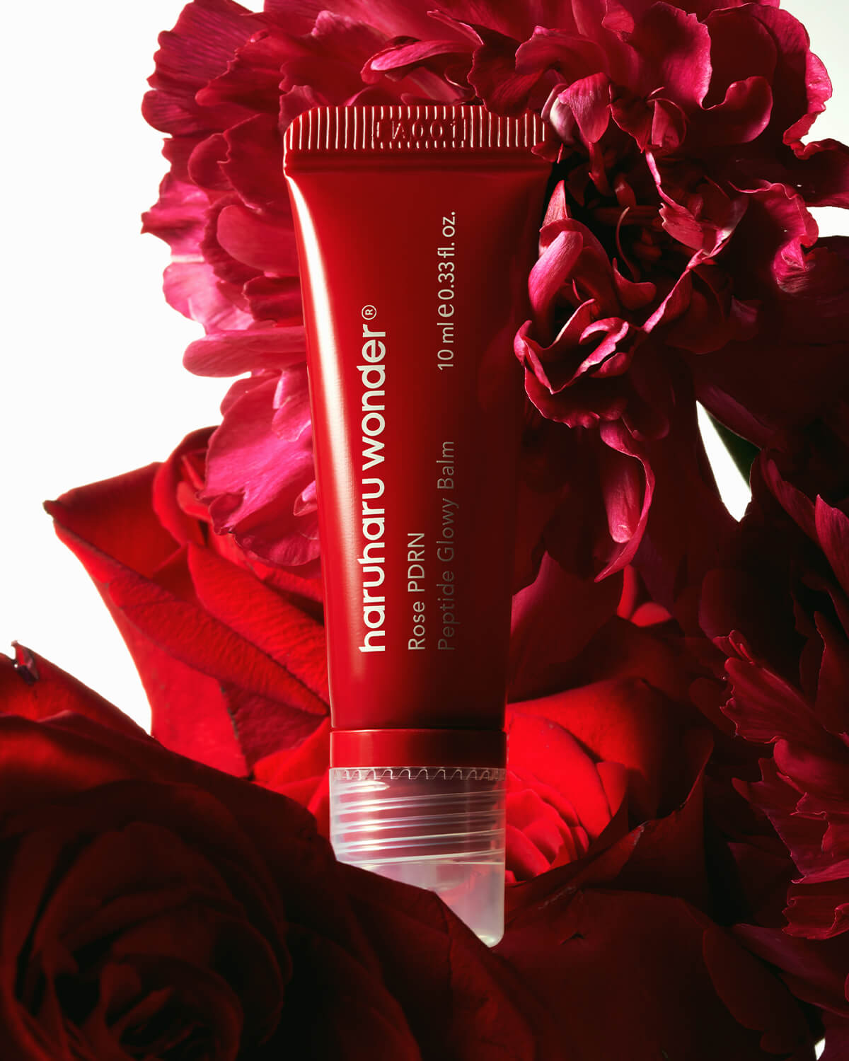 Haruharu Wonder Rose PDRN Peptide Glowy Balm tube nestled among vibrant red rose petals.