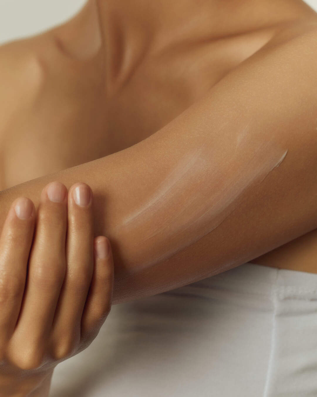 Close-up of smooth white moisturizing body lotion being applied to a person's shoulder.