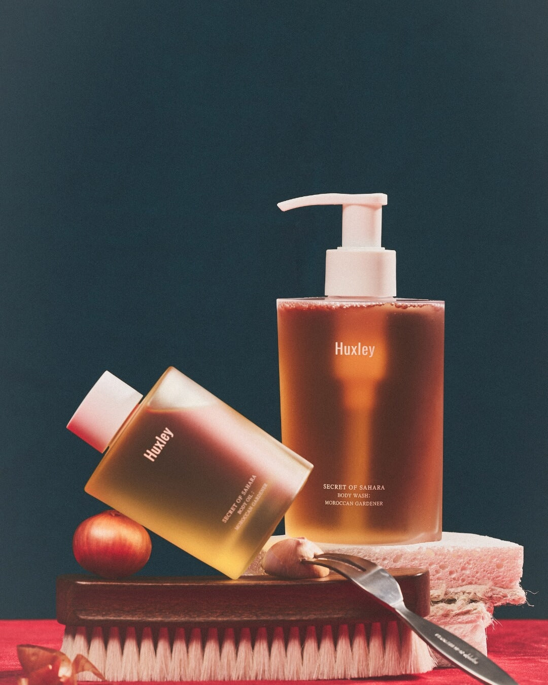 Huxley Moroccan Gardener body wash and body oil bottles displayed with a massage brush.