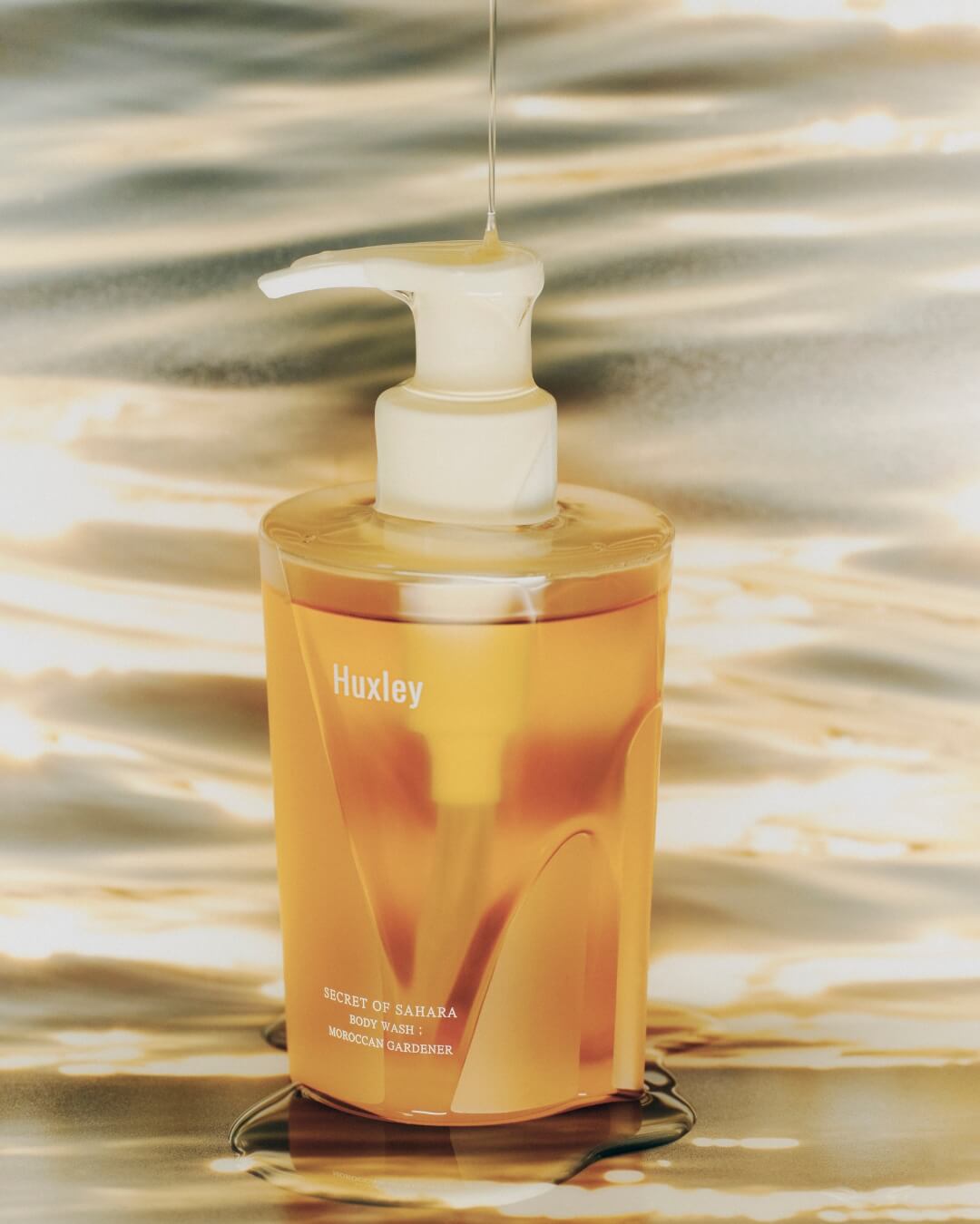 Huxley Moroccan Gardener body wash bottle on a reflective golden water surface.