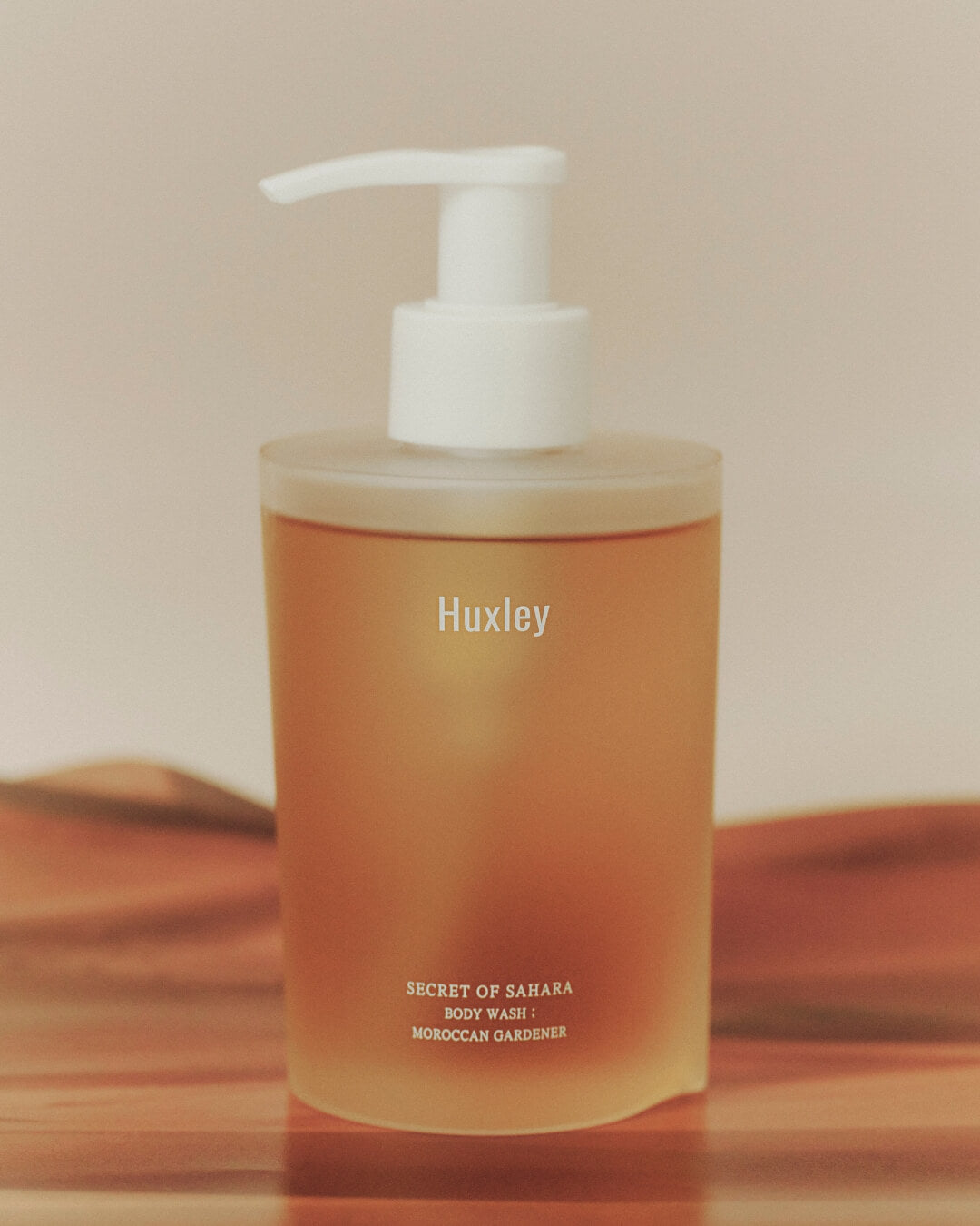 Huxley Secret of Sahara body wash bottle in warm, minimalist studio lighting.