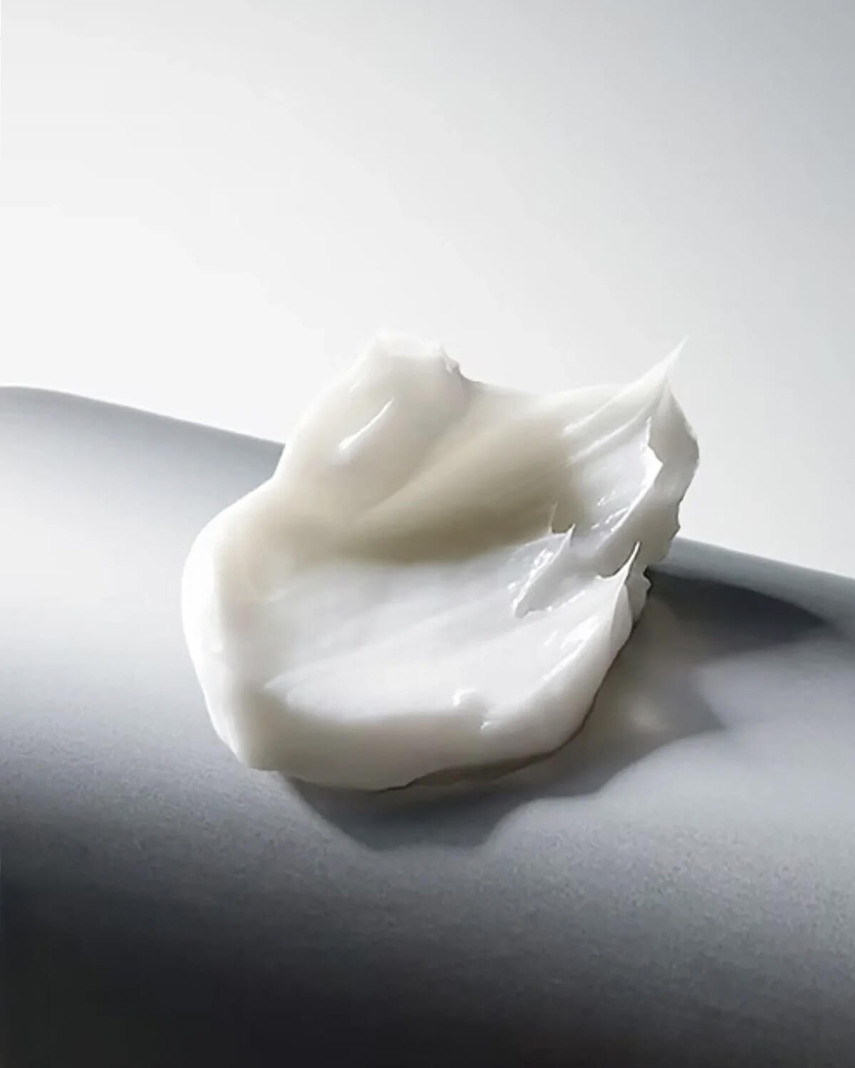 A scoop of the thick, white, moisturizing Cellinol-5 Cream is shown in a close-up texture shot on a gray background.