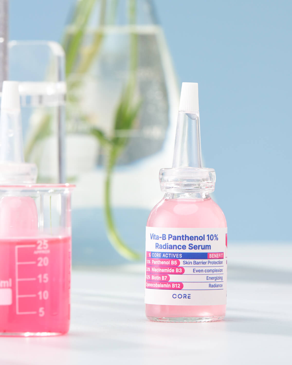 The serum bottle is placed on a white surface in a laboratory-style setting, next to a beaker containing a deep pink liquid, against a light blue background.