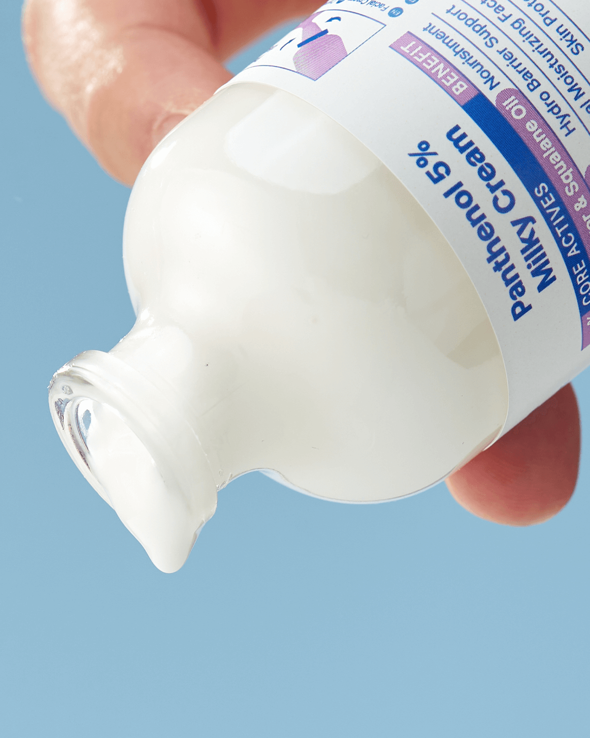 An extreme close-up of the bottle's neck and a hand holding it, showing a thick drop of the white cream clinging to the rim of the bottle against a blue background.