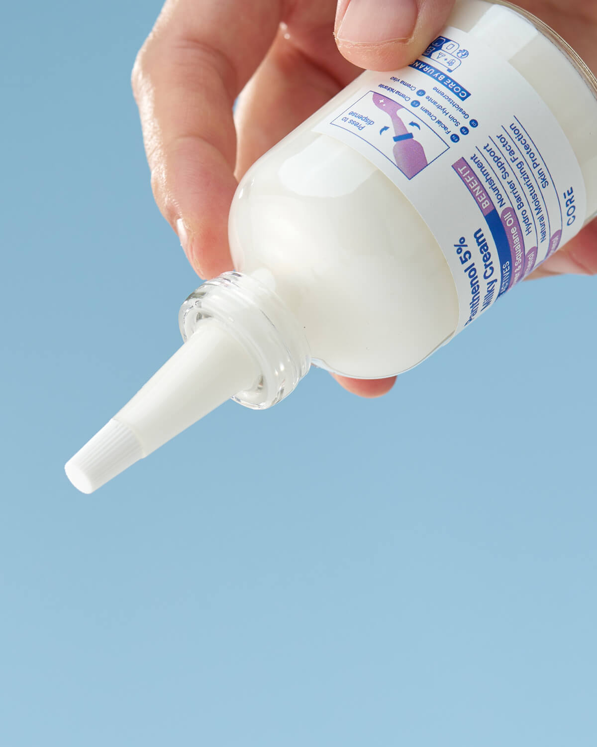 A hand holds the bottle upside down, ready to dispense the product, against a clear blue background. The label on the bottle is visible.