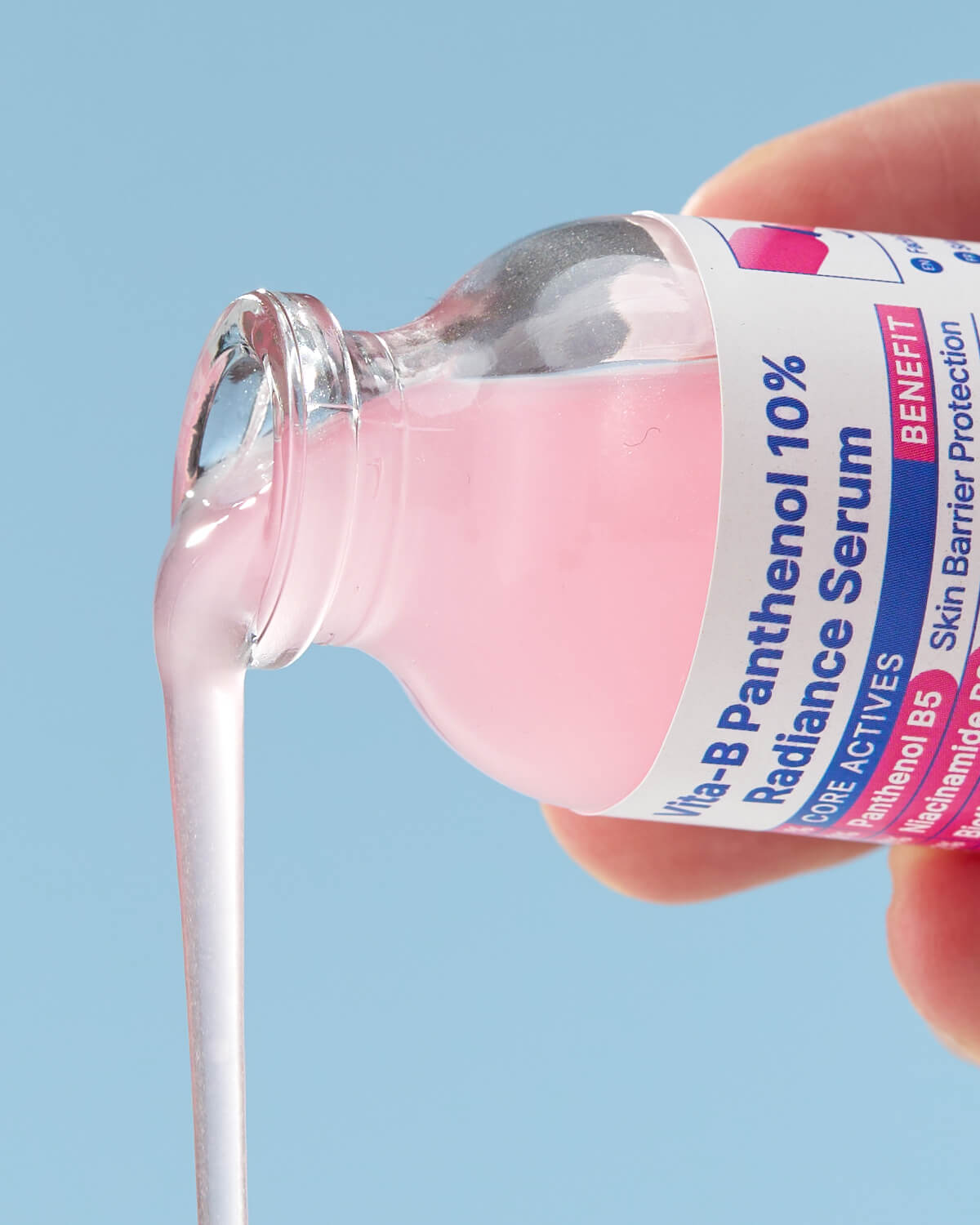 A close-up shot of the vibrant pink serum being poured out of the bottle in a thick stream, with the product label visible.
