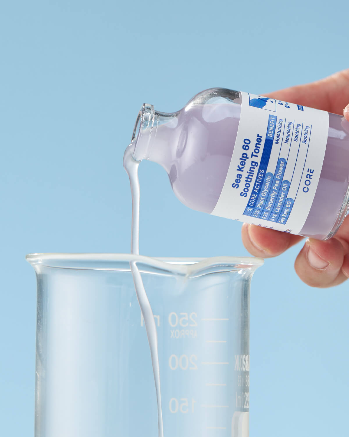 A stream of the pale, lavender-colored toner is being poured from the bottle into a clear glass lab beaker.