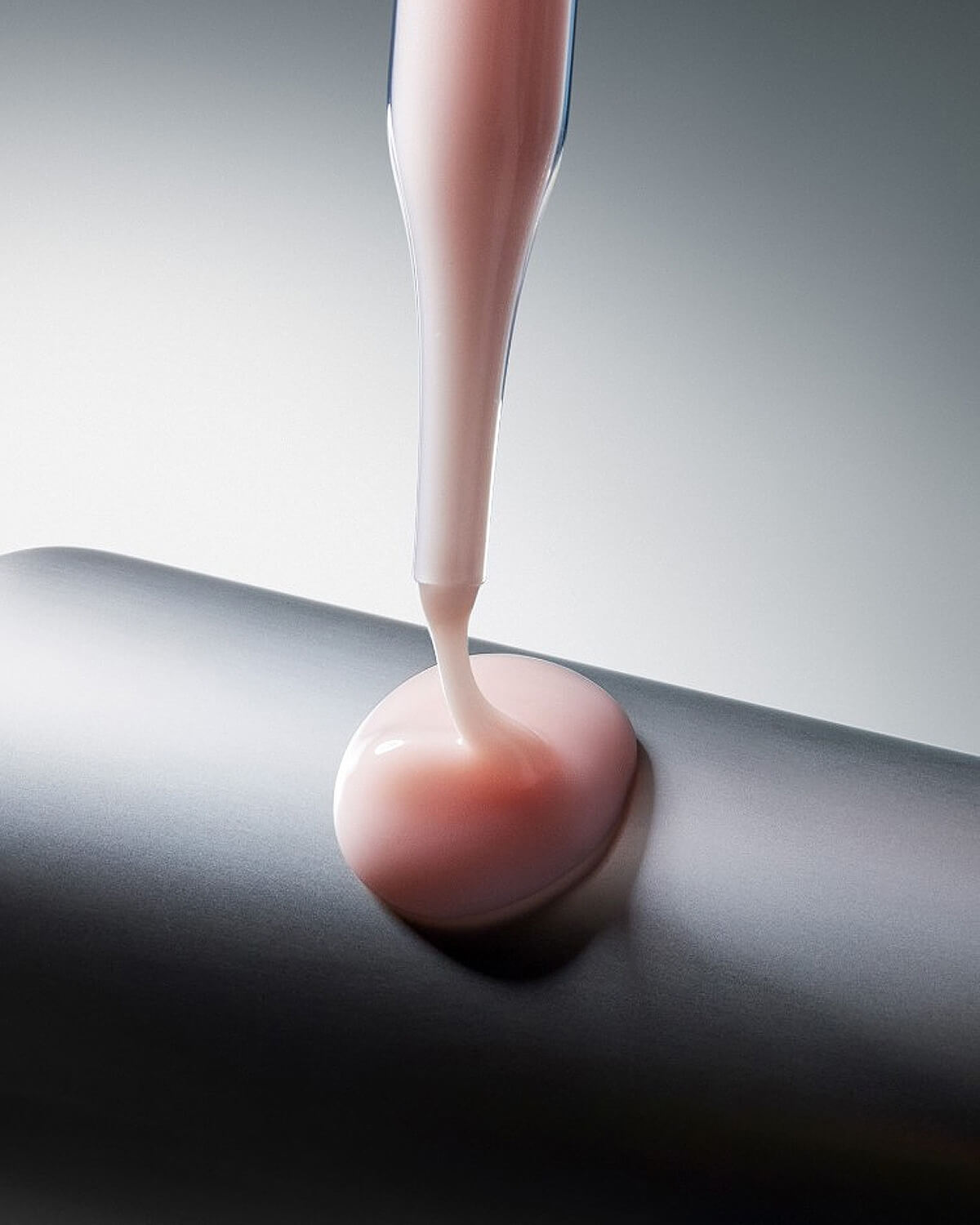 A close-up studio shot showing the thick, creamy texture of the pink Dexynol-16.3 Serum as it drips from a pipette onto a smooth gray surface.
