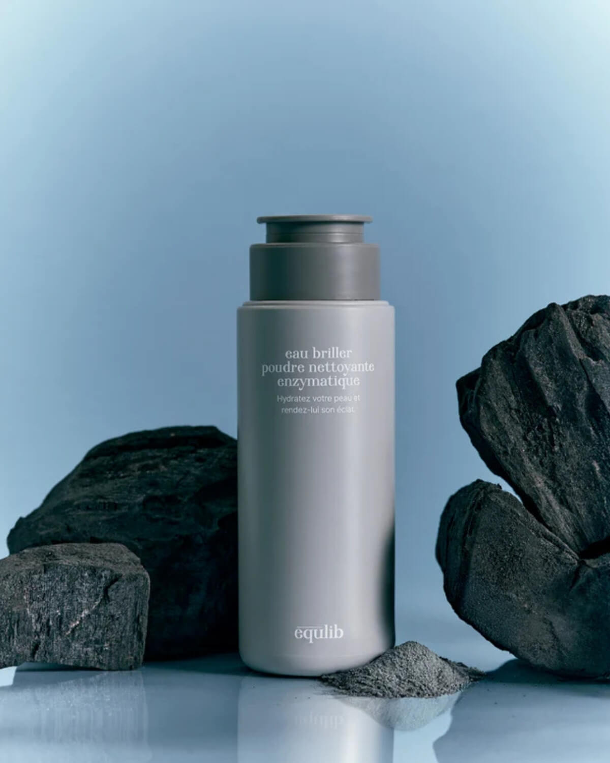Equlib enzyme powder wash bottle displayed with natural black charcoal stones on a light blue background.