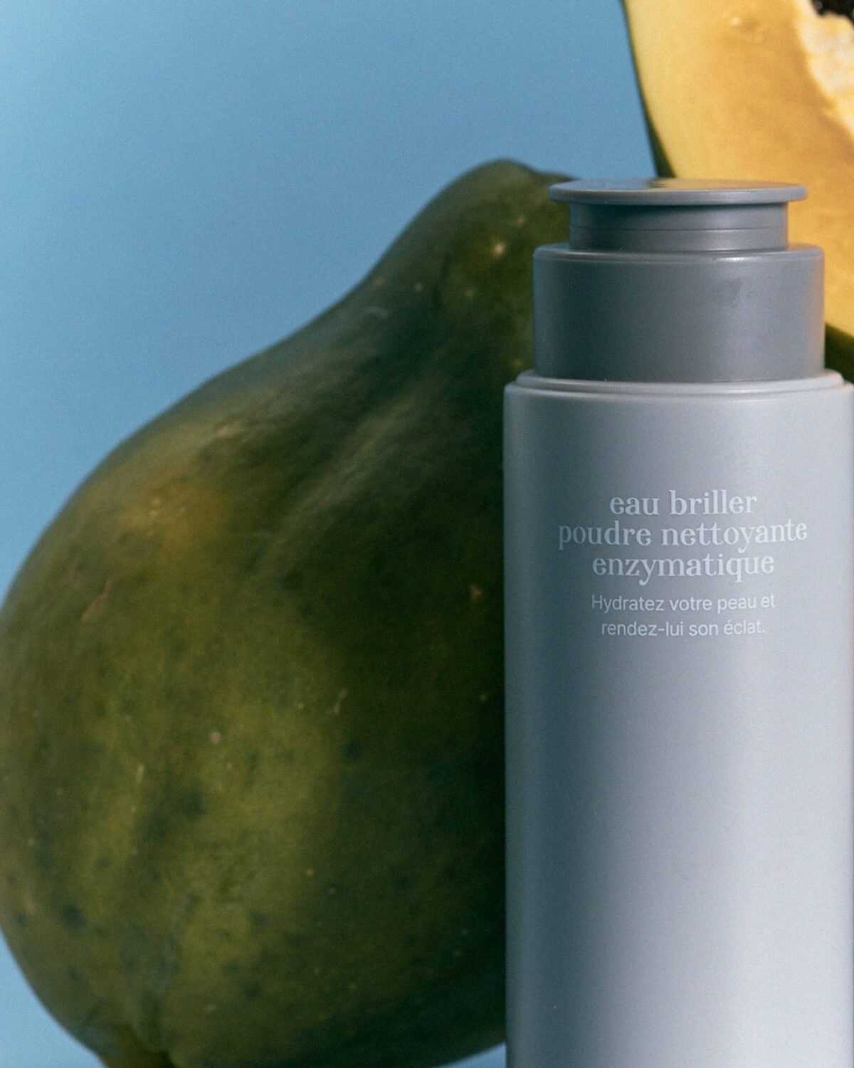 Close-up of Equlib powder cleanser bottle next to a fresh green papaya fruit, highlighting natural exfoliating enzymes.