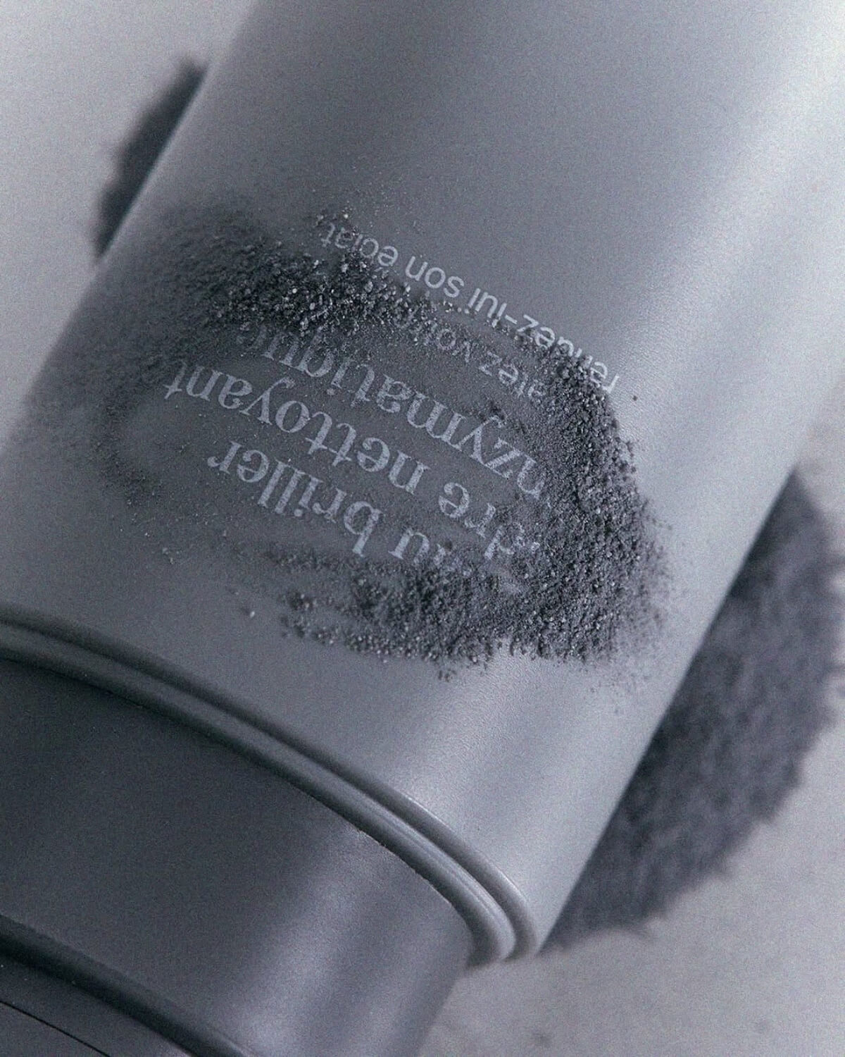 Close-up view of charcoal exfoliating powder textured over the grey Equlib enzymatic face wash bottle.
