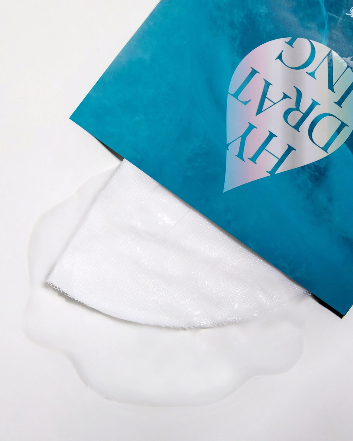 The white AIPPO Expert Hydrating Mask sheet folded next to its packaging, drenched in essence. Moisture-rich mask.