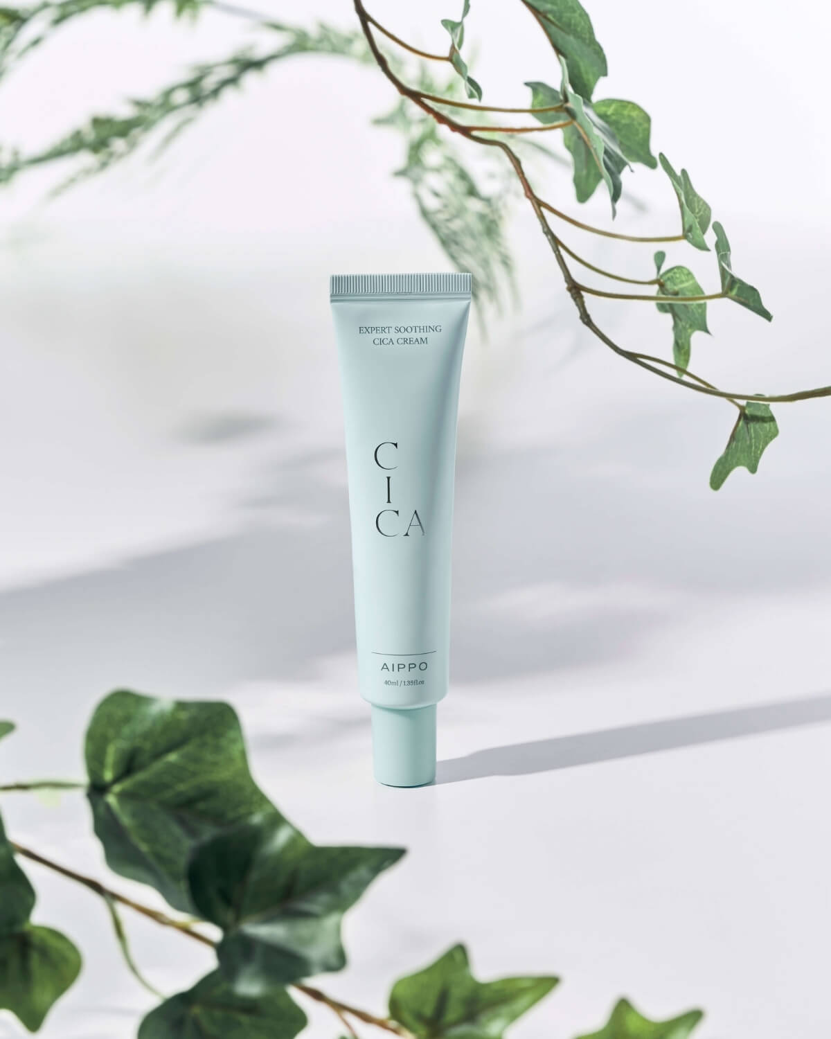 The Cica Cream tube is centered in a nature-inspired setting, surrounded by lush green ivy leaves and branches, with shadows creating a dappled effect.