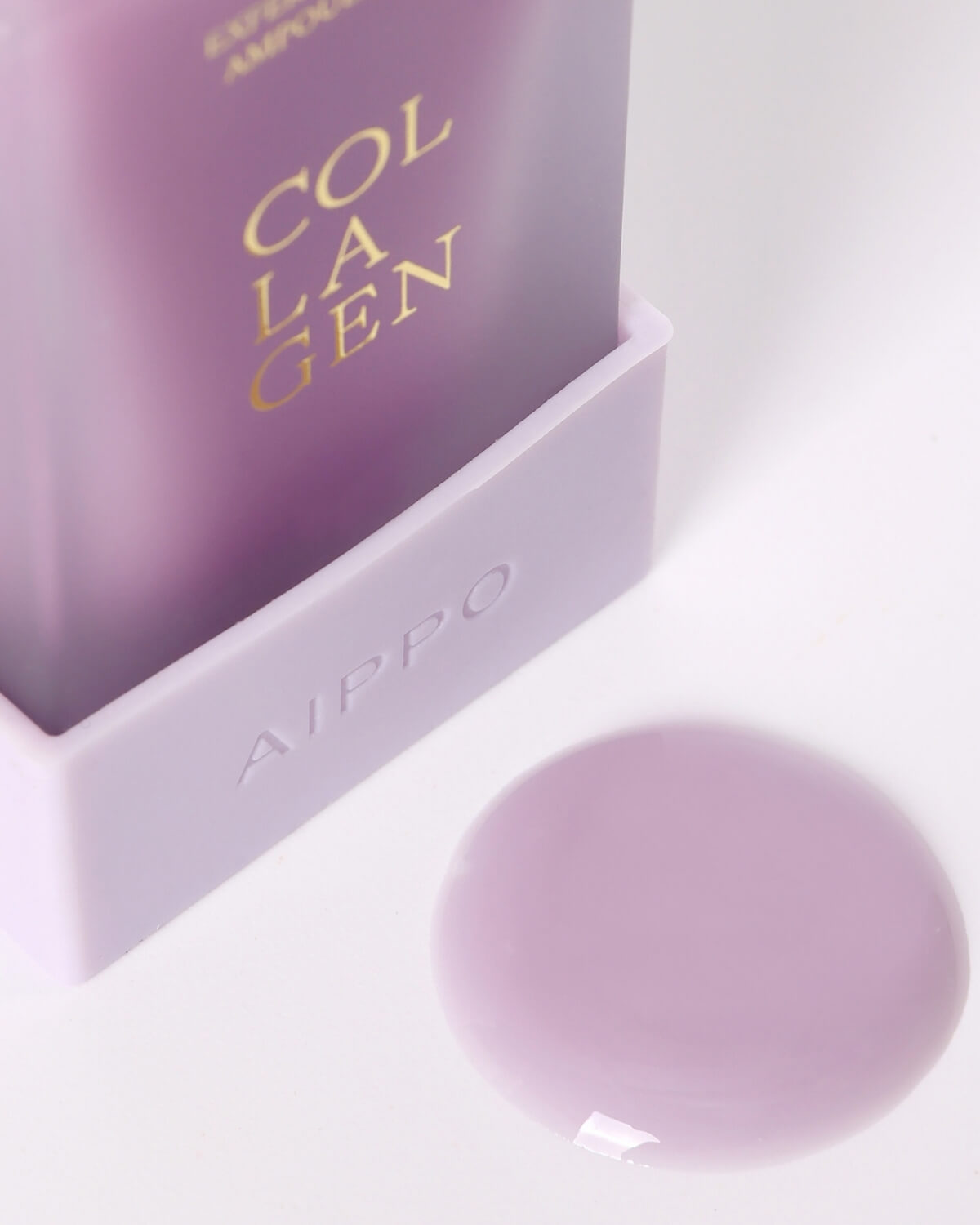 A close-up of the light purple base of the Aippo Collagen Ampoule Mask bottle, with a dollop of the smooth, violet-colored mask product puddled on the white surface next to it.