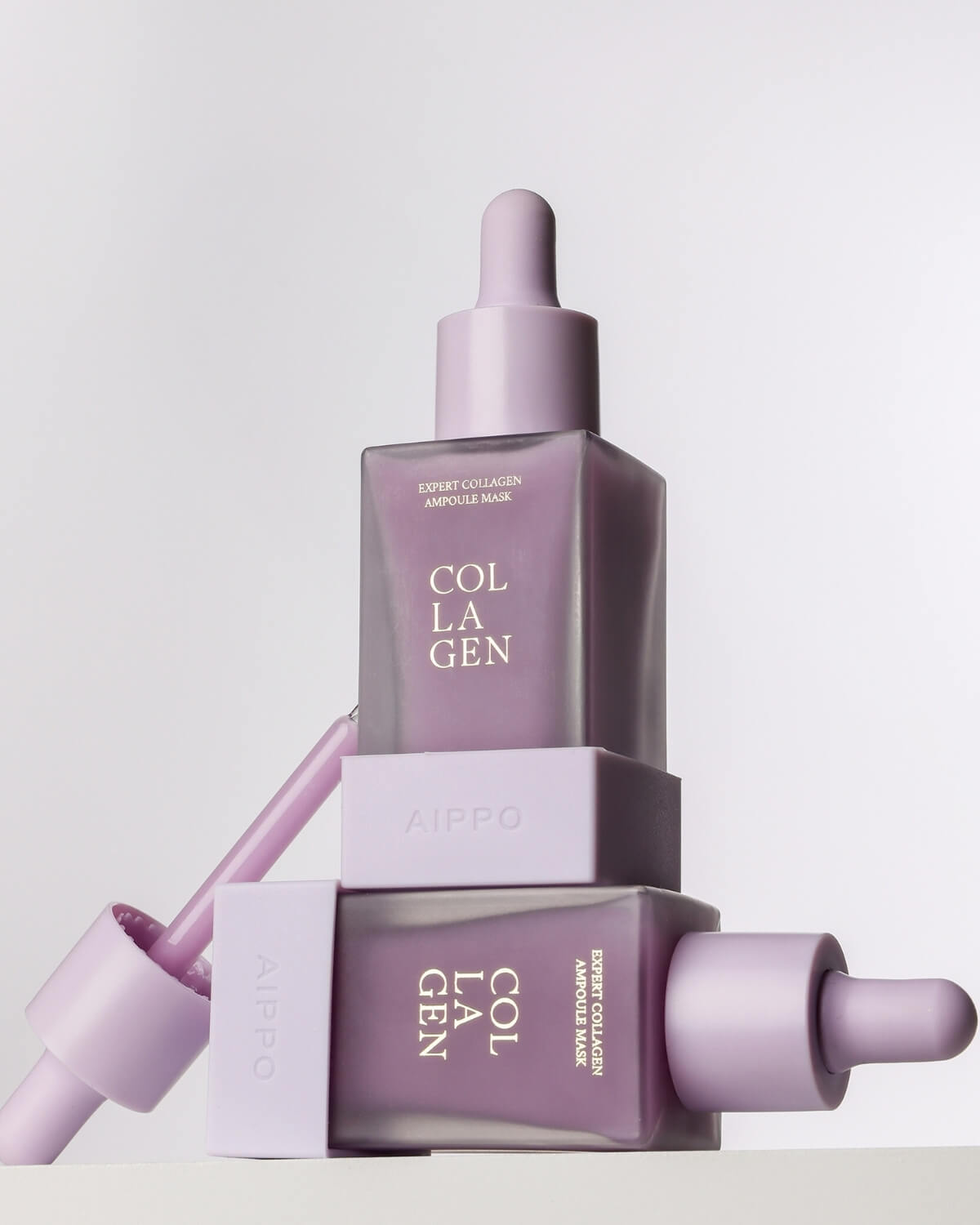 Two frosted purple Aippo Collagen Ampoule Mask bottles are stacked, one upright and one on its side, highlighting the contrast between the packaging and the rich purple ampoule inside.