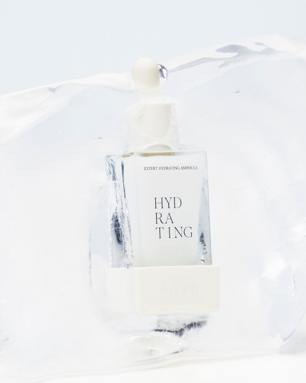 A close-up shot of two hands holding the dropper bottle of the Expert Hydrating Ampoule over a clear glass beaker, with a thick, hanging drop of the blue liquid poised to fall.