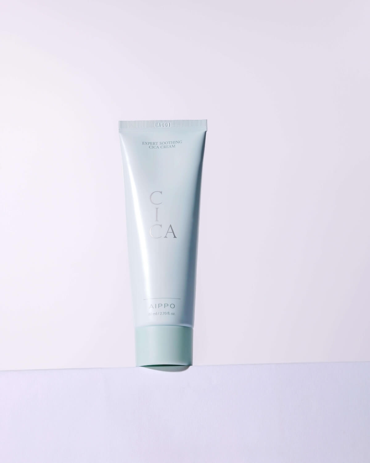 A clean, minimal studio shot of the Expert Soothing Cica Cream tube standing on a white surface with a subtle gradient background.