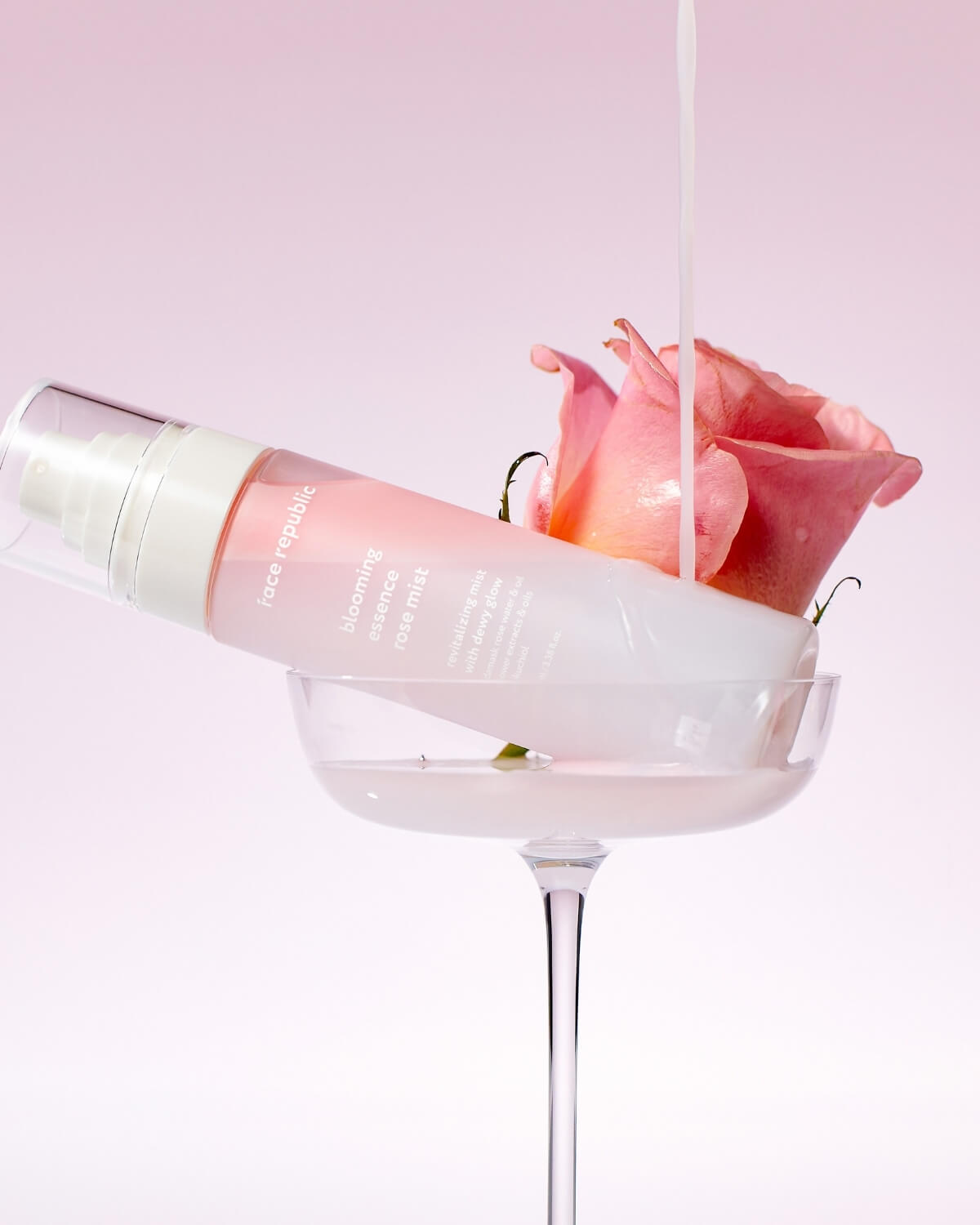 Artistic shot of Face Republic Rose Mist bottle in a glass with a rose and pouring liquid.
