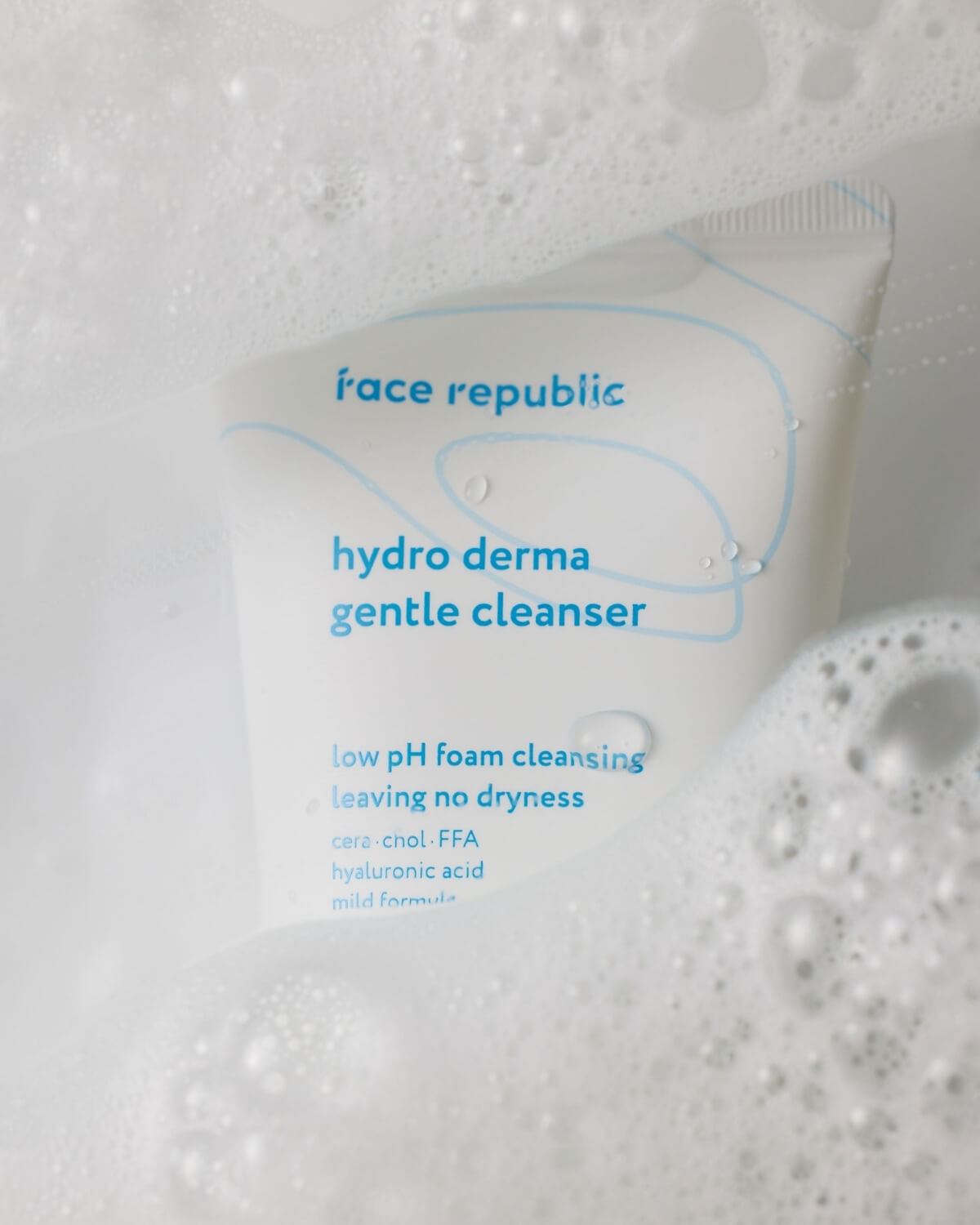 Close-up of Face Republic Hydro Derma Gentle Cleanser tube surrounded by soft white soap bubbles.
