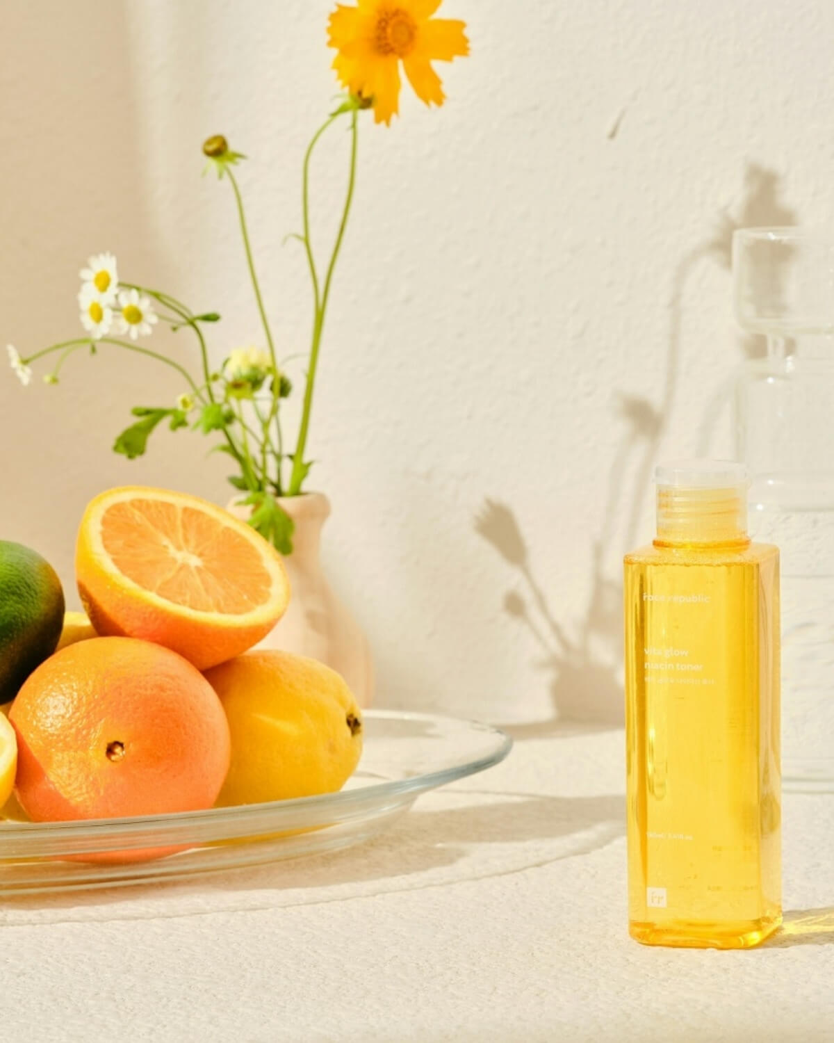 Face Republic Vita Glow Niacin Toner bottle styled with fresh citrus fruits and flowers.