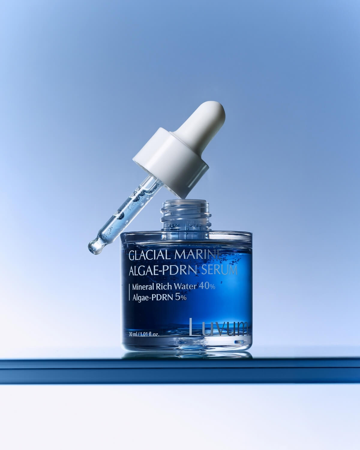 Open Luvum Glacial Marine Algae-PDRN Serum bottle with the dropper resting on top against a blue background.