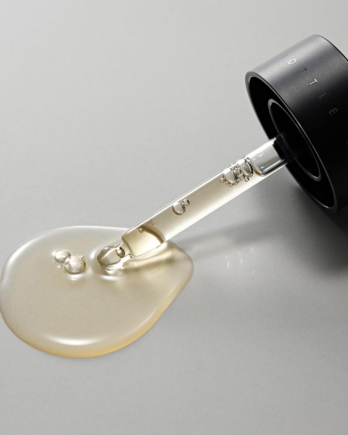 Close-up of a glass dropper releasing a clear, viscous drop of Glutathione & NMN Ampoule.