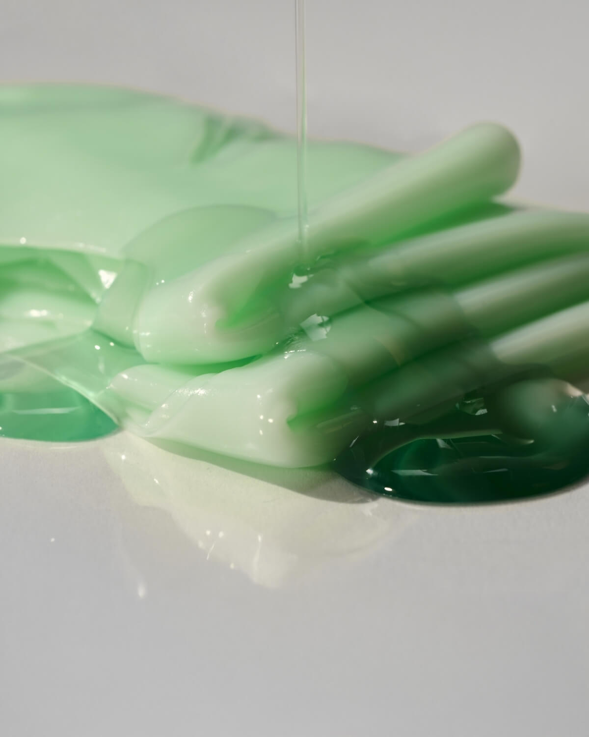 Close-up of a folded Luvum pale green hydrogel mask with clear, hydrating serum dripping over the texture.