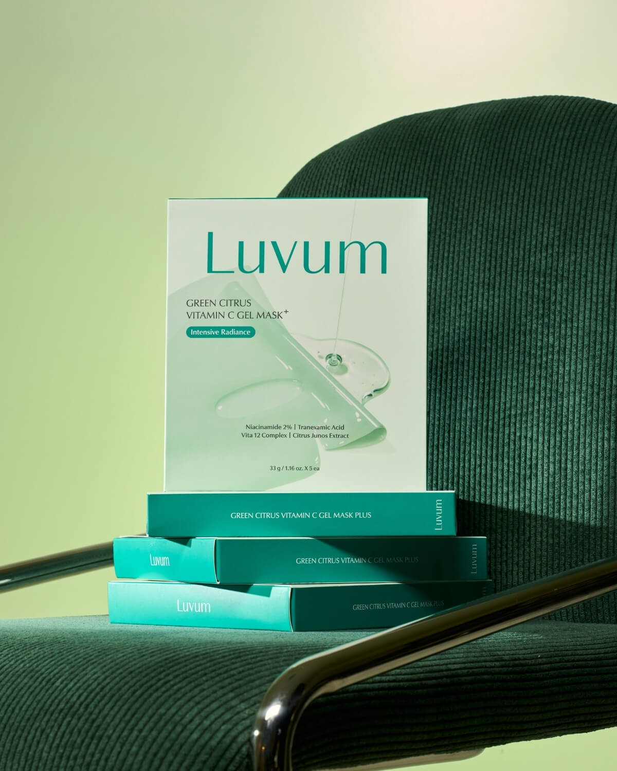 Pack of Luvum Green Citrus Vitamin C Gel Mask boxes balanced neatly on the cushion of a dark green corduroy chair.