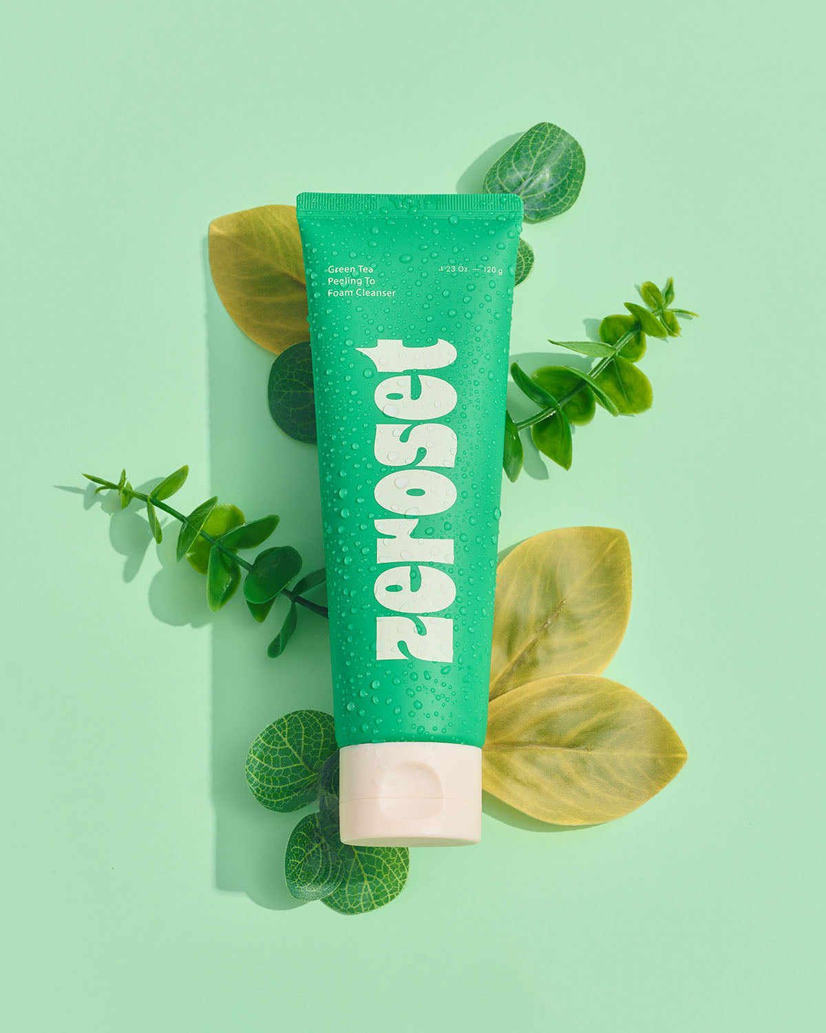 Zeroset green tea peeling to foam cleanser tube surrounded by fresh green botanical leaves.