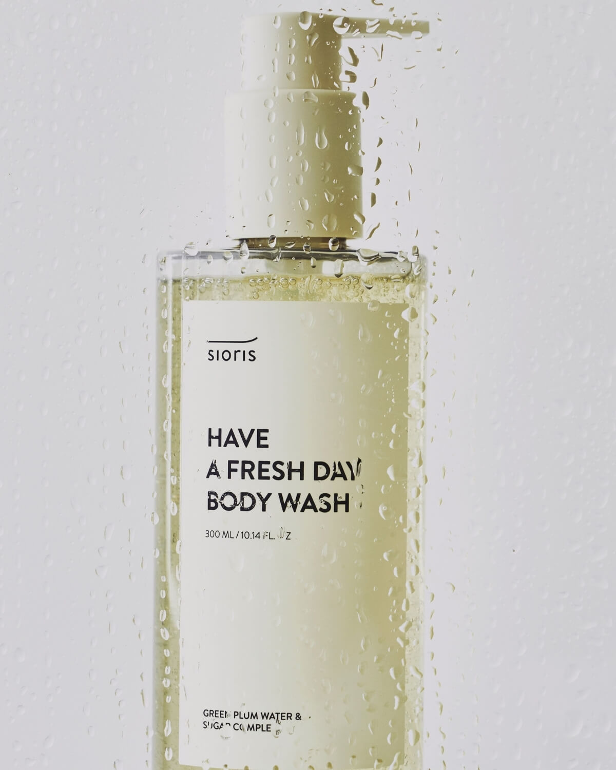 Sioris Have a Fresh Day Body Wash bottle seen through a glass pane covered in fresh water droplets.