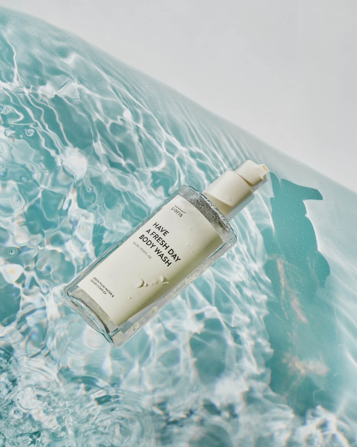 Sioris Have a Fresh Day Body Wash bottle floating in clear, rippling turquoise pool water.