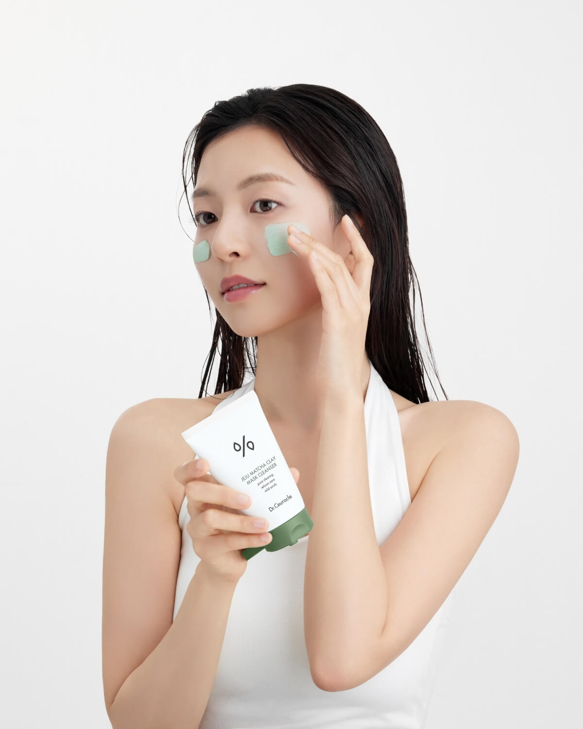 Woman applying Dr. Ceuracle Jeju Matcha Clay Mask Cleanser to her face while holding the tube.