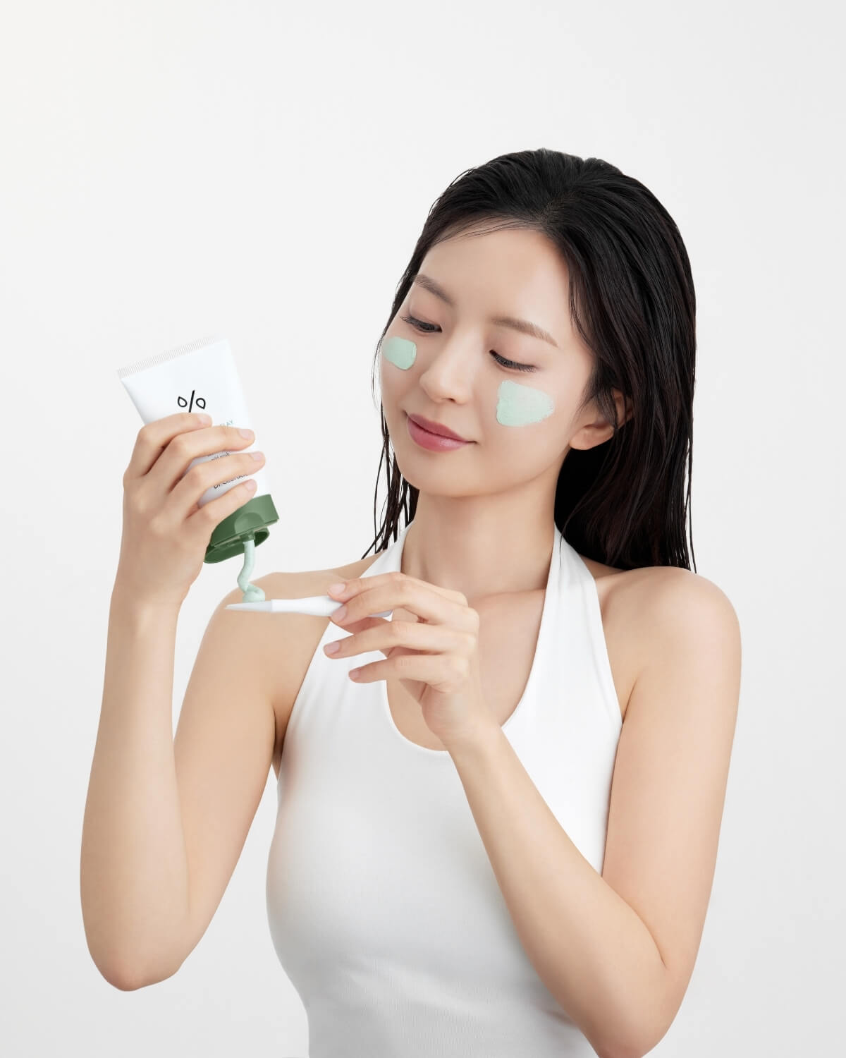 Woman squeezing green clay mask from Dr. Ceuracle tube onto a spatula for face application.