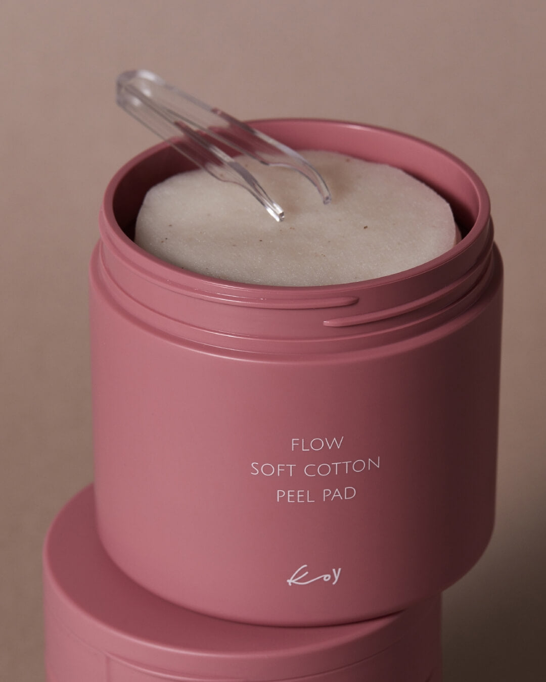 Open pink container of Koy Flow Soft Cotton Peel Pad with white facial pads and clear skincare tweezers.