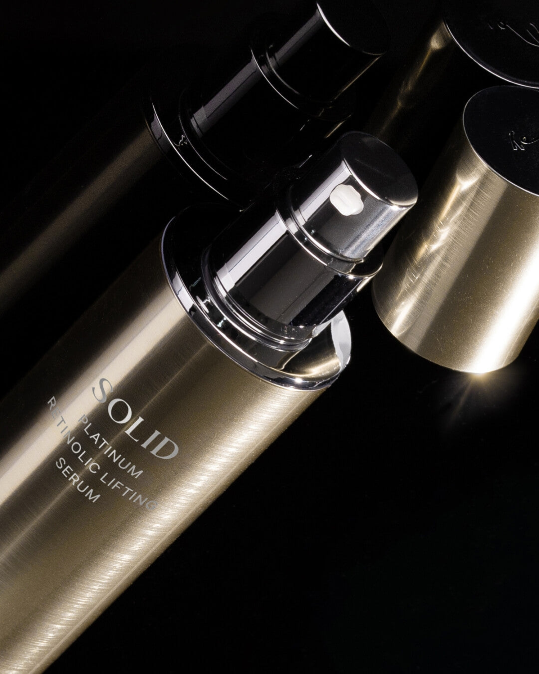 Close-up of the sleek gold Koy Solid Platinum Retinolic Lifting Serum pump on a reflective black surface.