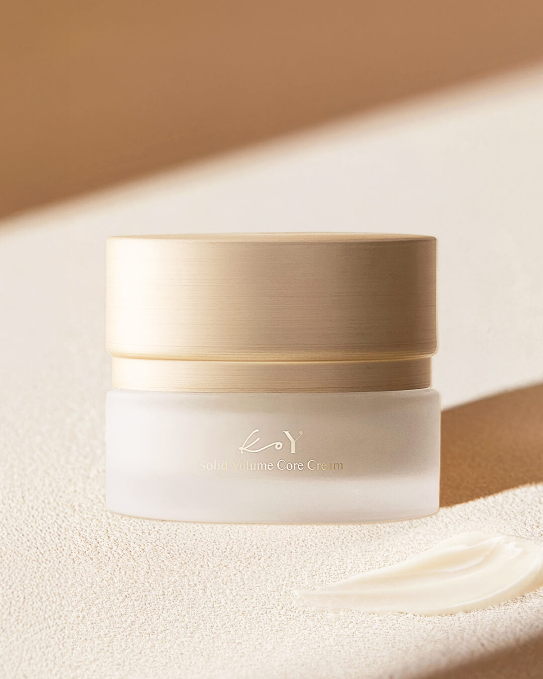 Koy Solid Volume Core Cream jar resting on a textured surface next to a smooth swirl of anti-aging face cream.