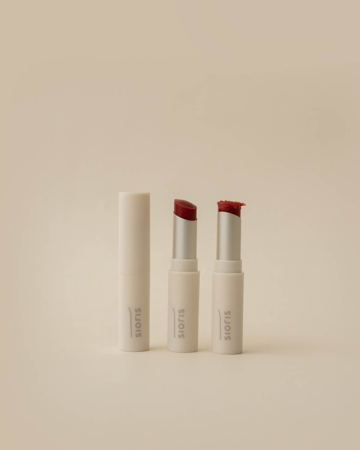 Three Sioris lip balm tubes standing upright, showcasing a closed cap, a clean balm bullet, and a textured cream top.