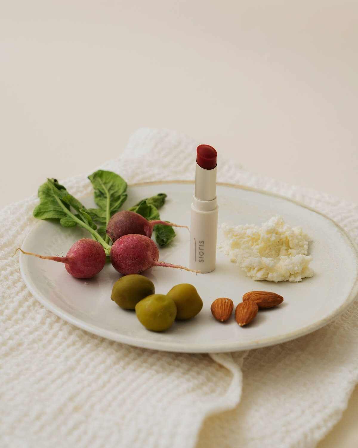 Sioris LipSafer Color Balm Reddish on a plate with healthy ingredients like fresh radishes, olives, and almonds.