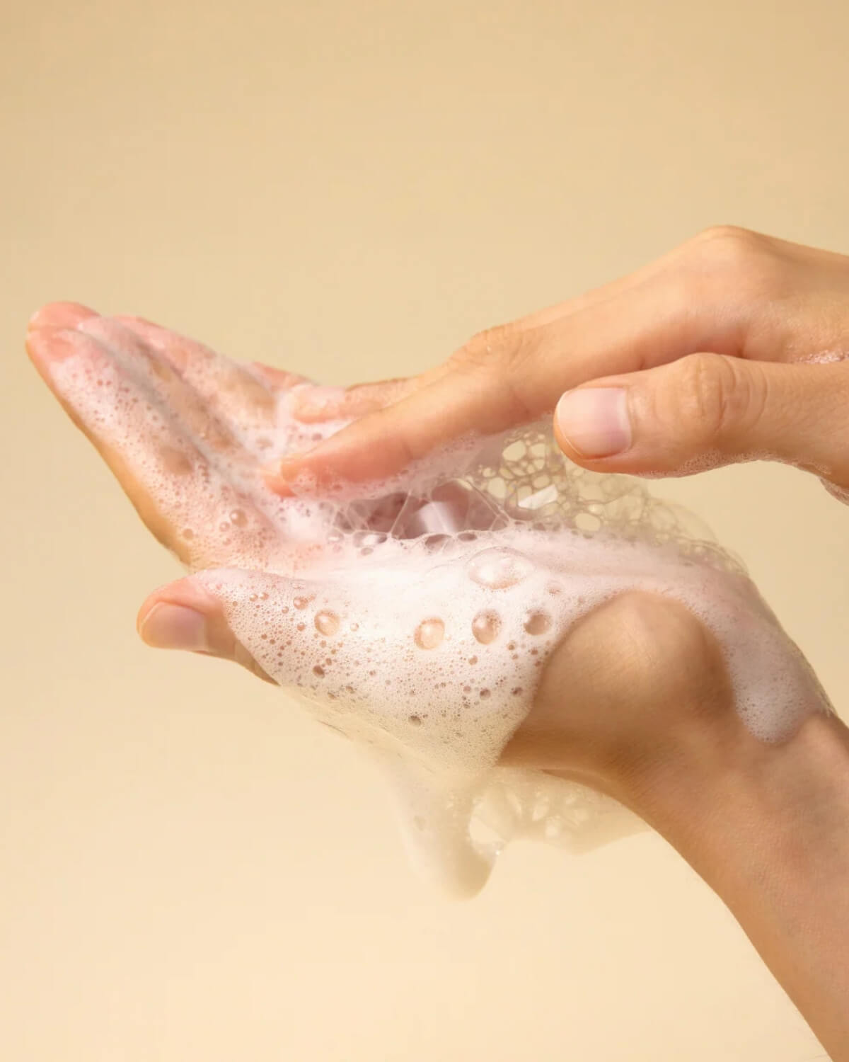 Close-up of a person’s hands lathering the cleanser into a rich, bubbly white foam.