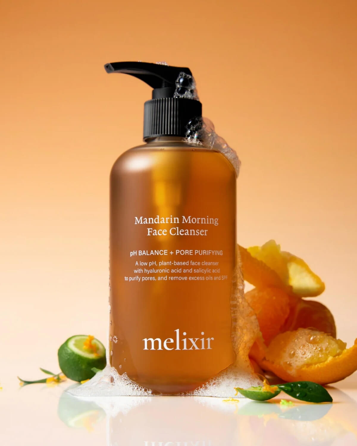 The cleanser bottle surrounded by fresh orange peels and citrus slices with soapy suds at the base.