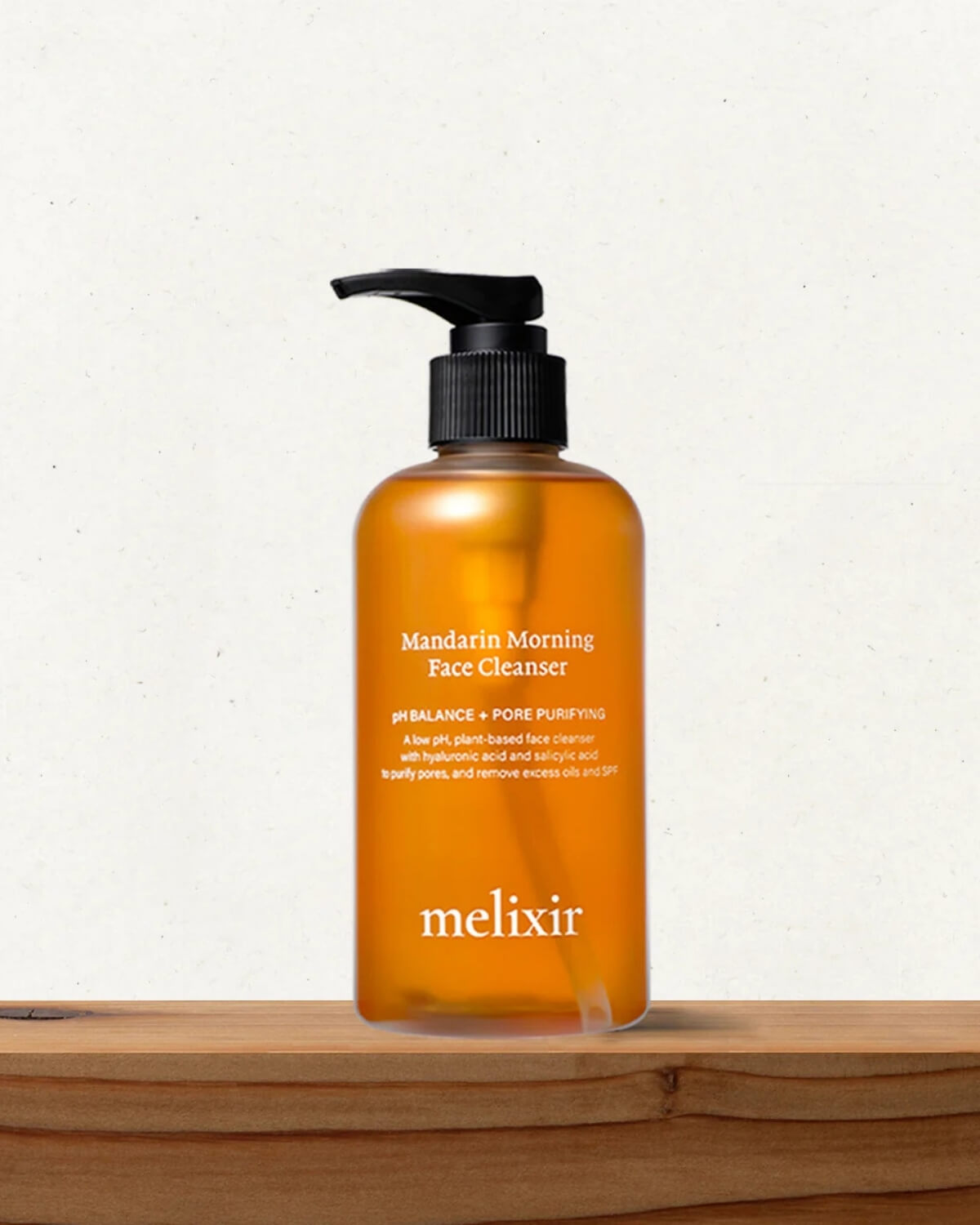 The Melixir cleanser bottle sitting on a rustic wooden ledge against a speckled off-white wall.