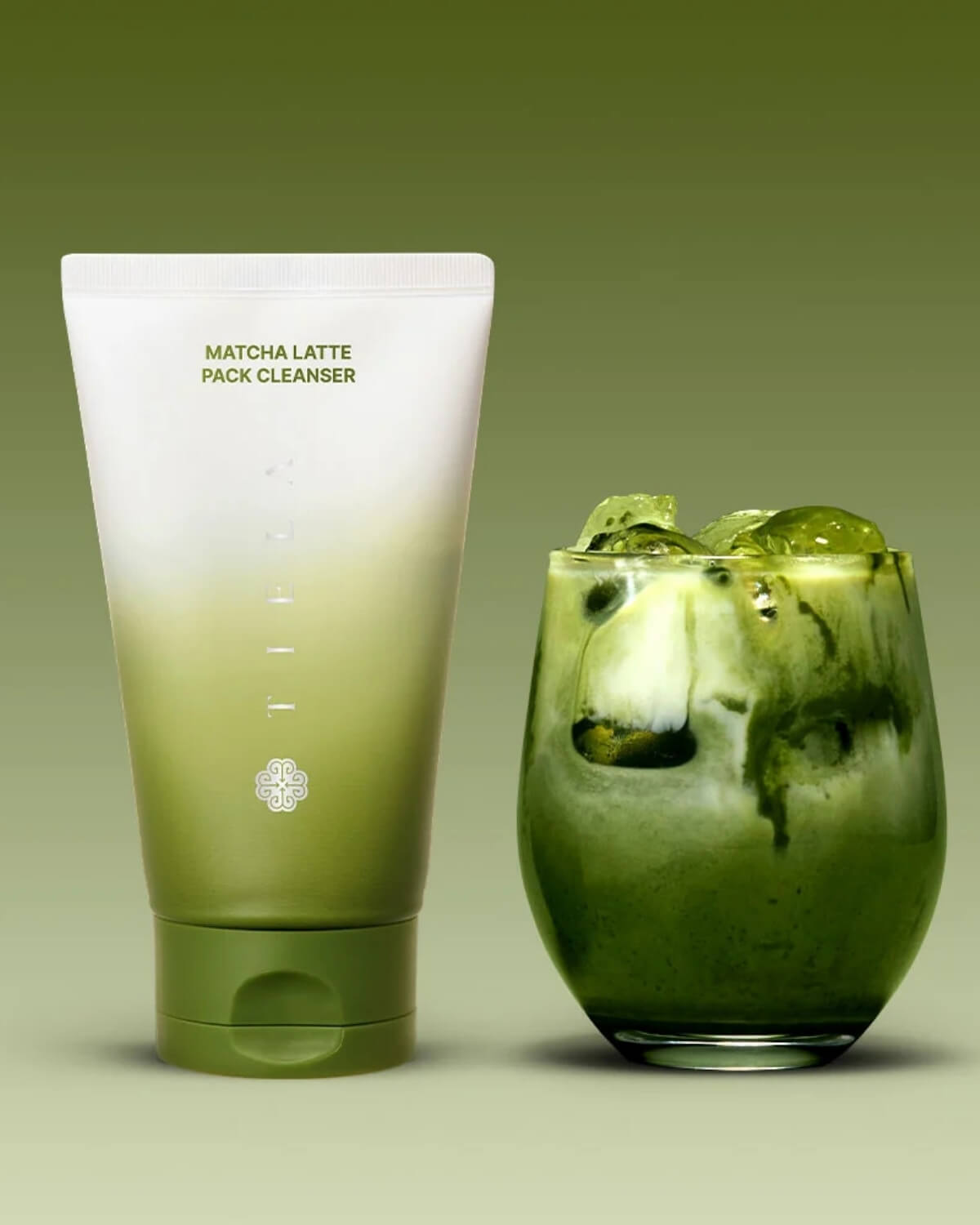 Tiela Matcha Latte Pack Cleanser tube standing next to an iced green tea matcha drink.
