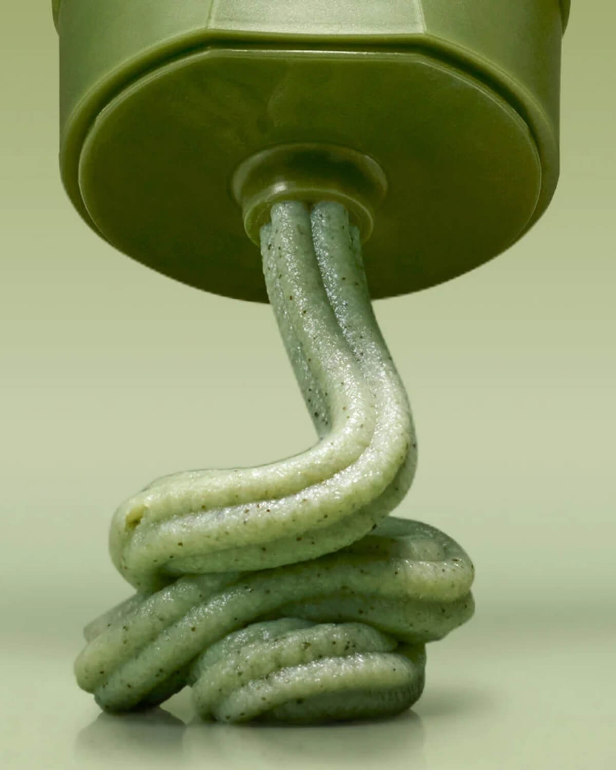 Close-up of green matcha face mask paste squeezing directly out of a green tube nozzle.