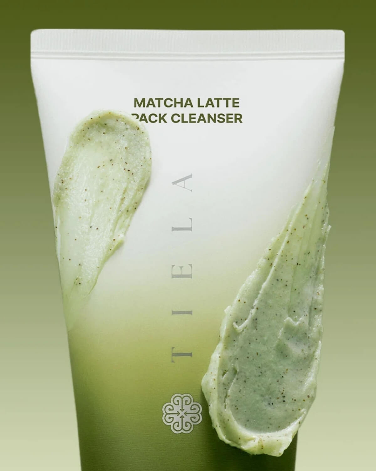Close-up of Tiela Matcha Latte Pack Cleanser tube with green mask texture swatched over it.