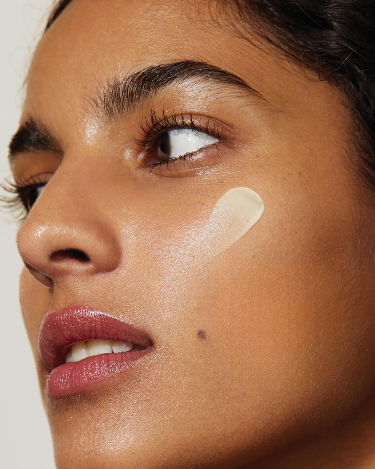Close-up of a person's face with clear skin, featuring a small swipe of cream or sunscreen on their cheek.