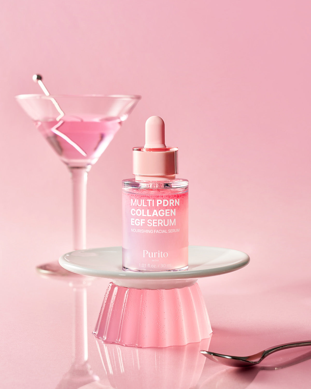 Purito Multi PDRN Collagen EGF Serum bottle on a white pedestal with a pink cocktail in the background.