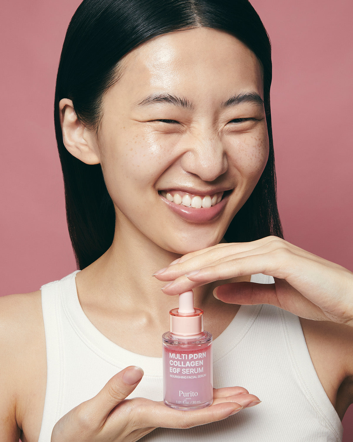 A woman laughing while holding a bottle of Purito Multi PDRN Collagen EGF Serum in her palms.