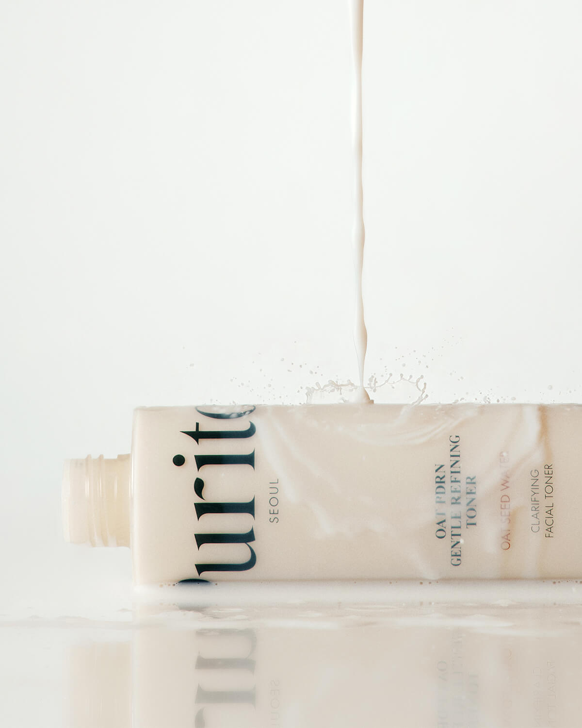 A milky liquid stream splashing onto the side of a toner bottle lying horizontally on a reflective white surface.